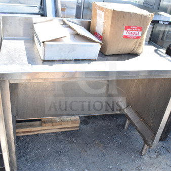Stainless steel counter with shelving, used condition. Markings indicate "Fragile" on cardboard boxes on top.