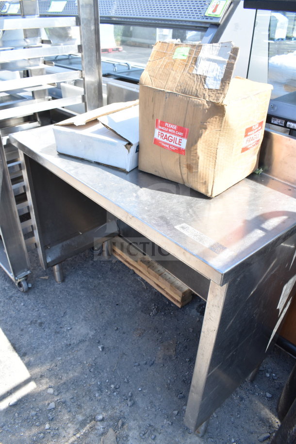 Stainless steel counter with visible wear, sturdy legs, and under-shelf. Boxes labeled "Fragile" on top.