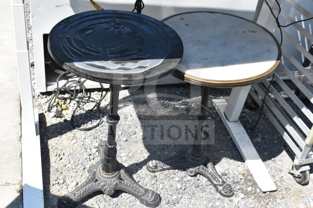 Three various tables; one black round, one marble-top round on ornate metal bases, and one white framework table.