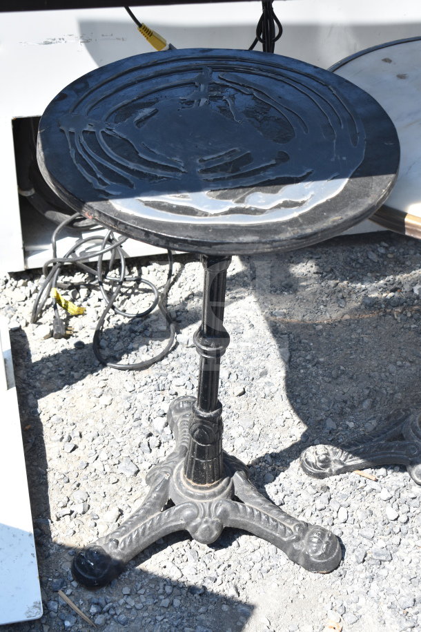 Cast iron round table with ornate base and weathered surface finish, outdoor setting.