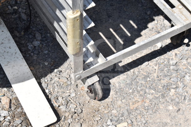 Commercial pan transport rack with metal frame, multiple slots, and heavy-duty casters, showing wear and outdoor use.
