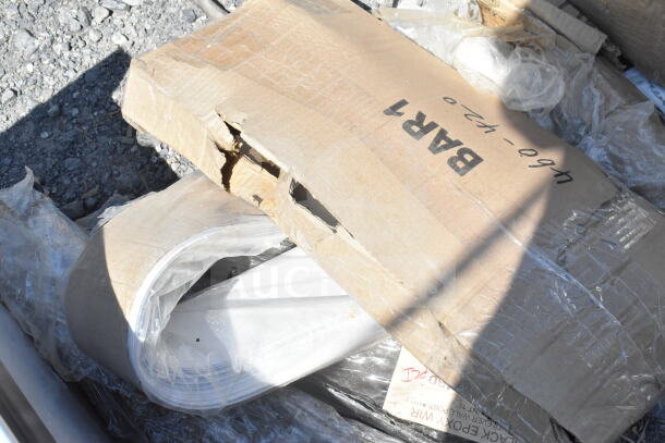 Box with visible damage containing Tuxton bowls, baking pan, and shelf liners in plastic wrap on gravel surface.