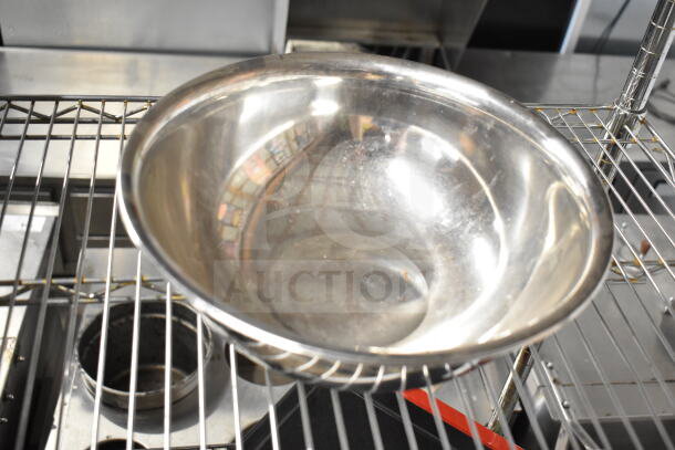 3 various metal bowls on a wire rack, shiny surface, used condition, suitable for kitchen or restaurant use.
