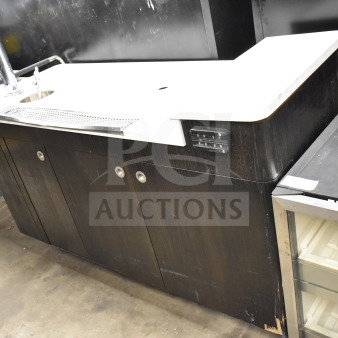 Portable bar with white countertop and dark wood base, featuring a faucet and storage cabinets. Slight wear visible on edges.