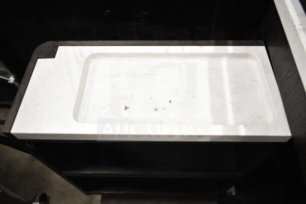 Marble-topped portable bar with a recessed surface, showing slight wear and minor debris, set on a dark wooden frame.