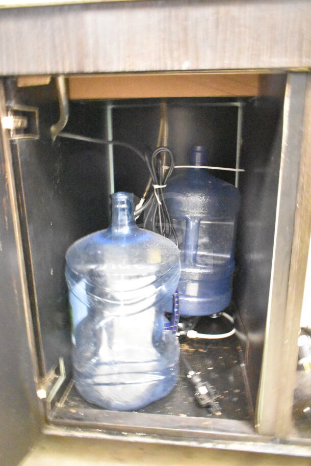 Portable bar interior showing storage space, two large water containers, and electrical wiring. Appears used.