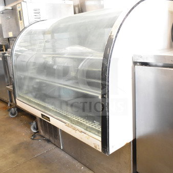 Delfield commercial deli display case, curved glass, floor style, visible wear, mounted on wheels, branded label intact.