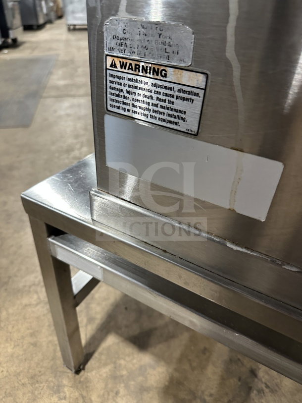 Stainless steel electric tilting steam-jacketed kettle on legs, with warning label. Excellent for commercial kitchens.