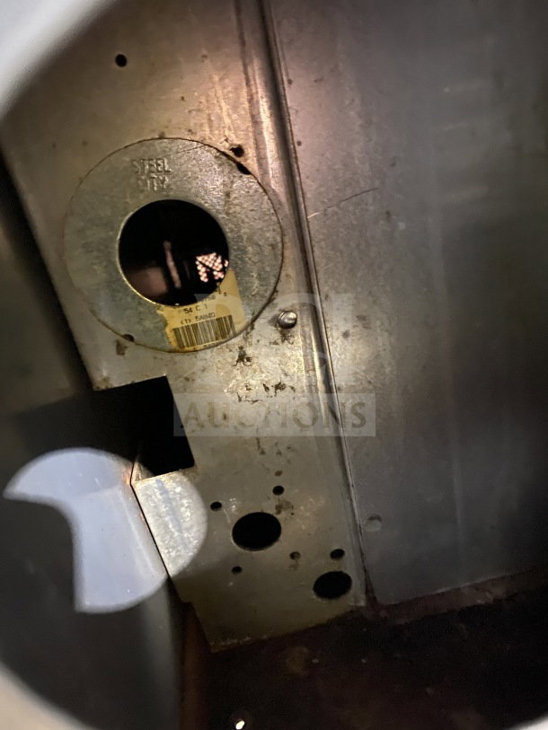 Metal enclosure interior with a circular cutout labeled "Steel City." Visible rust around cutout. Yellow sticker below.