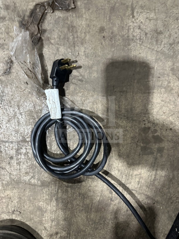 Black electrical power cord with three-prong plug, coiled on a concrete surface.