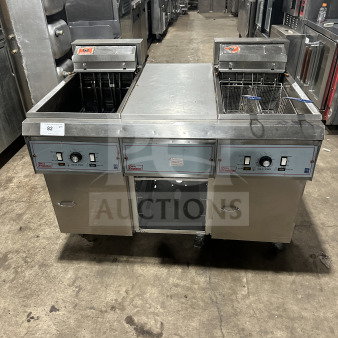 Pitco Frialator 2-bay stainless steel deep fat fryer system with center pan cabinet, backsplash, and basket hanger on casters.
