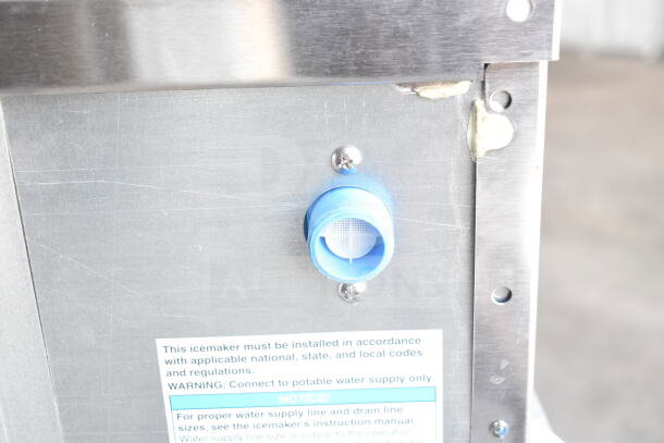 2025 Hoshizaki AM-50BAK ice machine showing water supply connection and instruction label on metallic surface.