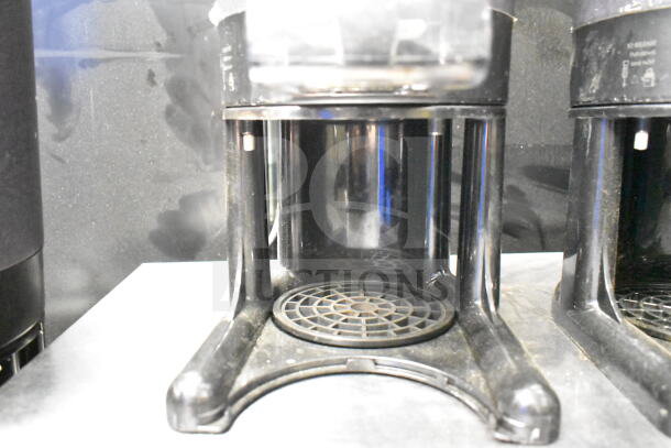 Pair of countertop beverage holder dispensers with black finish, grid pattern base, and release markings; used condition.