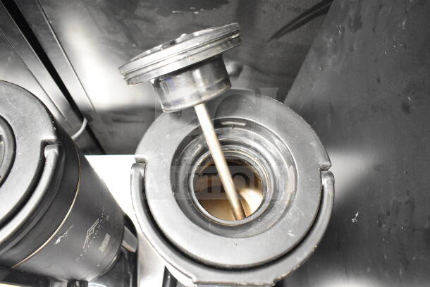 Two black countertop beverage holder dispensers, top view, metal stirring rod visible, showing interior and lid details.