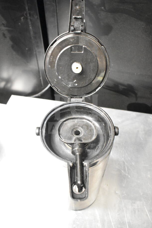 Alt text: Stainless steel air pot with open lid, showing interior mechanism. Slight wear visible. Suitable for holding hot beverages.