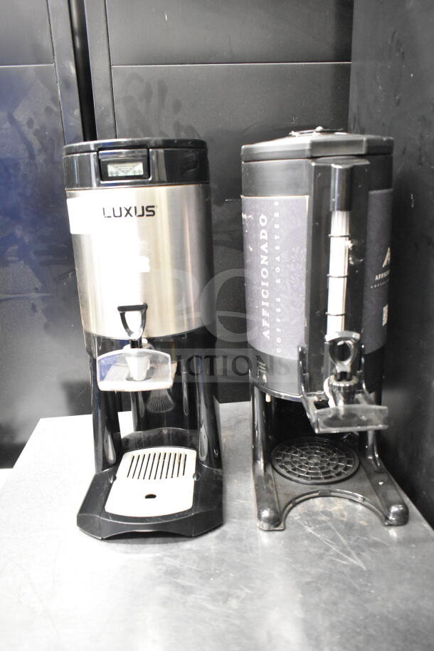 Pair of Luxus countertop coffee dispensers, stainless steel and black plastic, with drip trays. Visible branding includes "Luxus" and "Aficionado Coffee Roasters." Condition appears used.