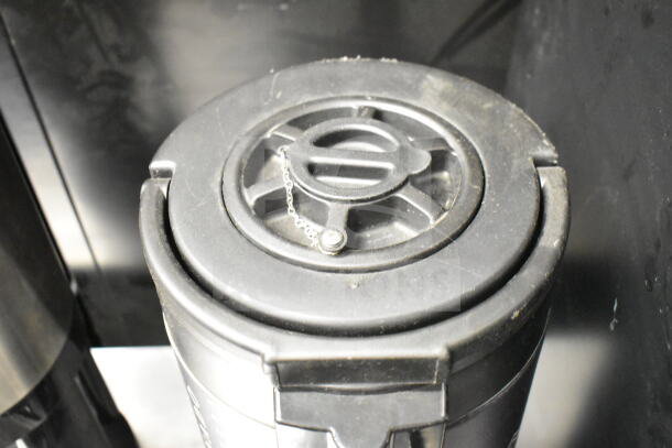 2 Luxus countertop coffee holder dispensers, black with lid and chain detail, in used condition.