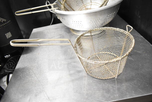 Metal colander and mesh strainer on stainless steel surface, used kitchen utensils in good condition for auction.