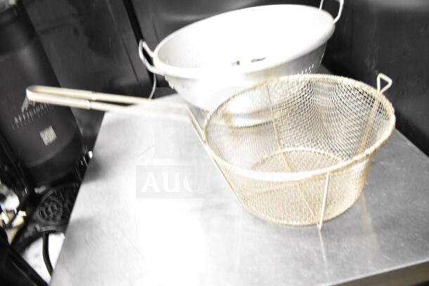 Metal colander and strainer on a stainless steel surface, part of an 8-item auction set. Handles visible, lightly used condition.