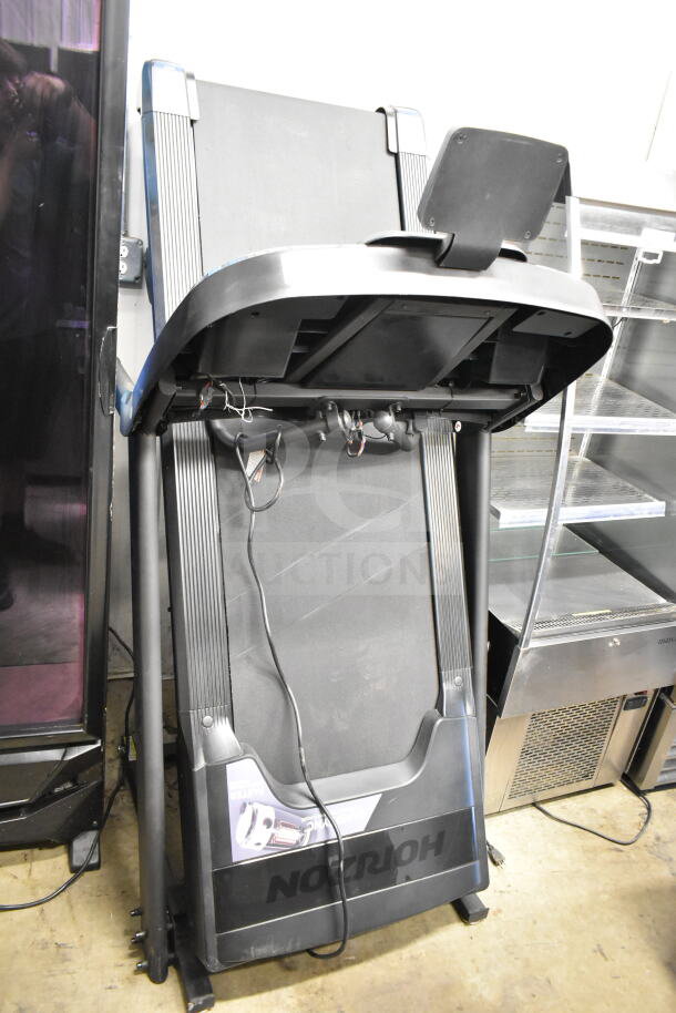 Horizon folding treadmill in good condition, black with visible power cord. Compact design, suitable for limited spaces.
