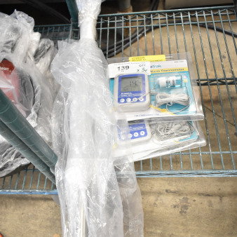 3 brand new items including 2 DeltaTrak thermometers in packaging and a wrapped wall rack on metal shelf.