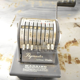 Vintage Paymaster Ribbon Writer check printer with metal lever, visible numeric dials for dollars and cents, and warning label; shows age-related wear.