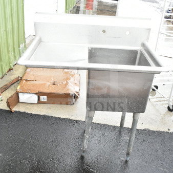 Commercial single bay sink with left side drain board, stainless steel, on legs, worn condition.