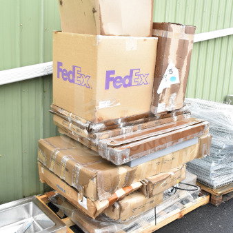 Stack of brand new scratch and dent items, including a table, in damaged FedEx boxes on a pallet.