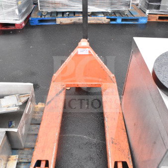 Orange pallet jack with visible wear, black handle, sturdy frame, suitable for lifting and moving pallets.
