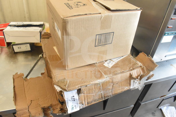 Cardboard boxes containing Koala Kare KB150-99 baby changing station liners and Lancaster Table & Seating Excalibur table base.