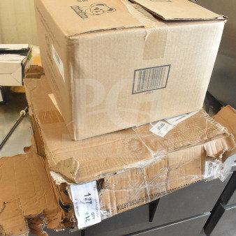 Cardboard boxes containing Koala Kare KB150-99 baby changing station liners and Lancaster Table & Seating Excalibur table base.