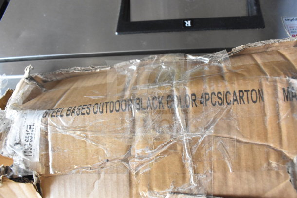 Damaged cardboard box containing Lancaster Table & Seating Excalibur 22" x 22" Cross Outdoor Table Base Plate, marked as "Steel Bases Outdoor Black Color 4Pcs/Carton."
