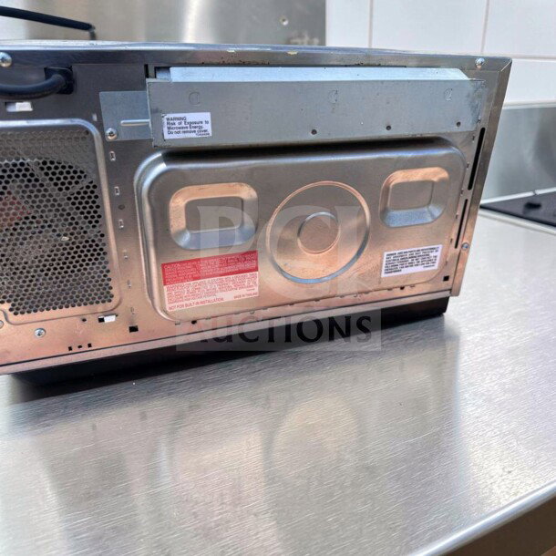 Sharp R-21LCFS commercial microwave oven, stainless steel, 1000W, dial control. Shown with visible safety labels, fully operational.