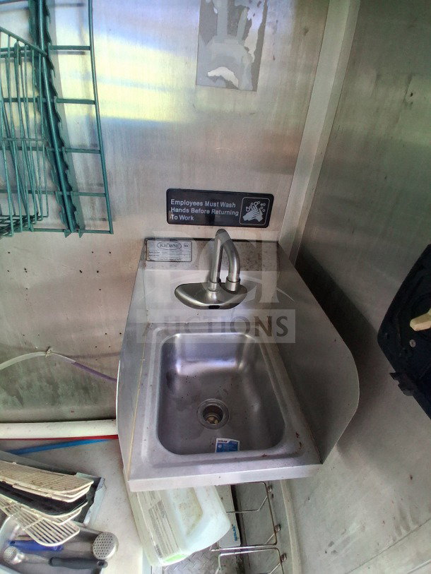 Stainless steel sink with faucet in a 2020 Diamond Cargo mobile kitchen. "Employees Must Wash Hands" sign above.