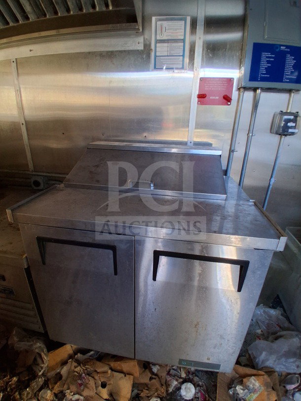 2020 Diamond Cargo 24' Custom Mobile Kitchen interior. Features stainless steel fridge, fire suppression controls, and cookline elements.