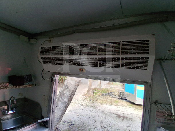 Interior view of a 2019 D&A Custom 24ft mobile kitchen trailer; features air curtain above door, sink, and shelving.