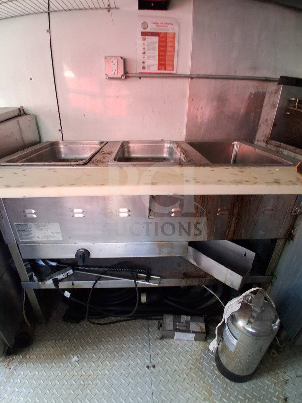 Interior view of a D&A Custom 2019 mobile kitchen with stainless steel serving trays and visible wiring. Clean and organized setup.