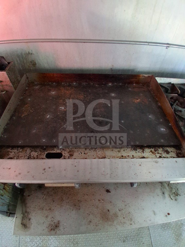 Interior of 2019 D&A Custom Mobile Kitchen, featuring a used griddle with visible wear, set against a metal wall.