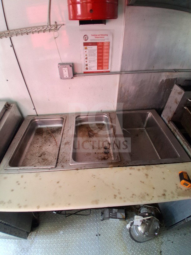 Interior of 24ft 2019 D&A custom mobile kitchen, featuring a stainless steel prep table with three compartments, showing wear.