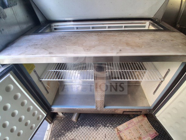 2019 Diamond Cargo mobile kitchen interior, showing refrigeration unit needing cleaning. Features wire shelves and durable build.