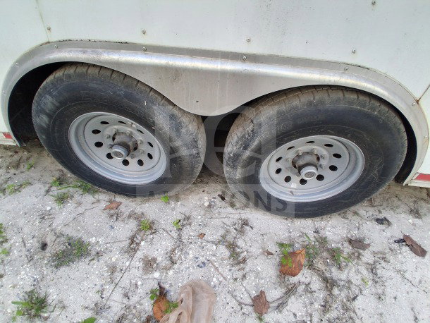 Dual wheels of a 2019 Diamond Cargo 24' mobile kitchen trailer, showing wear. Tires on sandy ground with some vegetation.