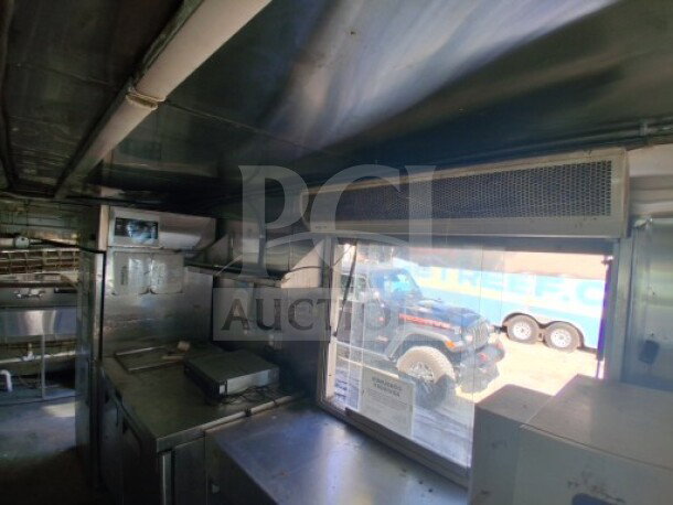 2019 Quality Cargo food trailer interior, featuring large order window, grease hood, fryers, griddle, cooktop, and refrigeration.