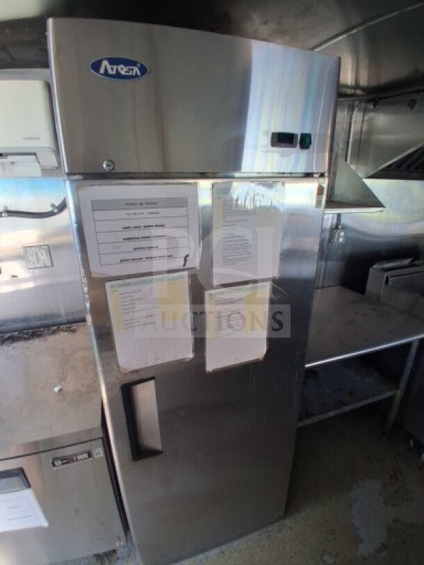 Commercial kitchen interior of 2019 Quality Cargo Food Trailer. Visible is a stainless steel refrigerator with brand logo "Arctic," various equipment, and a grease hood.