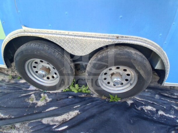 2019 Quality Cargo Food Trailer tires and wheels, dual axle, visible part of blue trailer body, metal trim detailing.