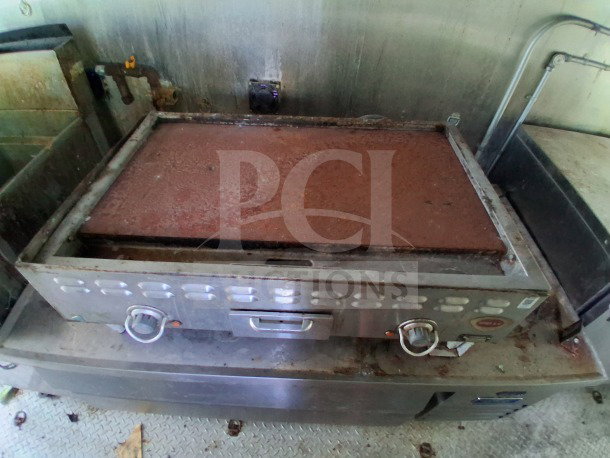 Rusty commercial-grade griddle inside the 2021 Haulmark 8.5' x 24' Mobile Kitchen Trailer, with visible piping and metal surface.