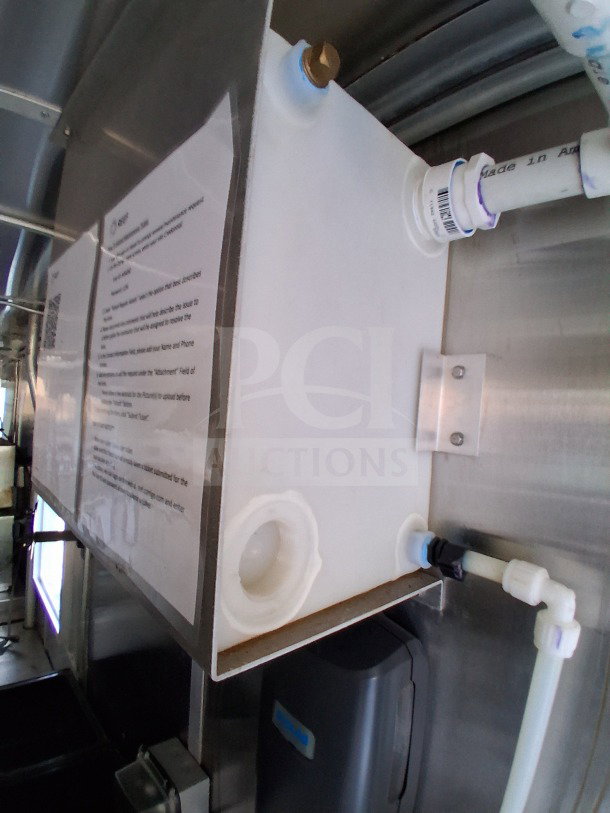 Interior view of 2021 Diamond Cargo 24' Mobile Kitchen showing plumbing and signage. Stainless steel and white pipes visible.