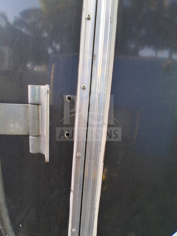Close-up of the 2019 Quality Cargo Food Trailer exterior, showing metal trim and hinge, with visible wear and small holes.