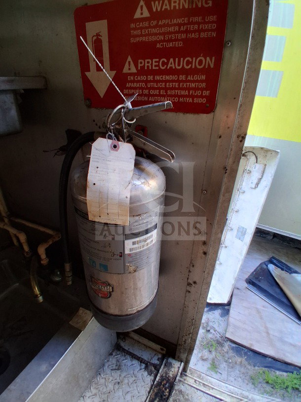 Fire extinguisher inside 2019 Quality Cargo food trailer, near warning sign. Extinguisher has a tag with usage instructions.