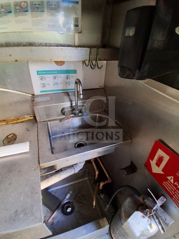 Interior view of 2019 Quality Cargo Food Trailer showing a small stainless steel sink with faucet, plumbing, and nearby fire extinguisher.