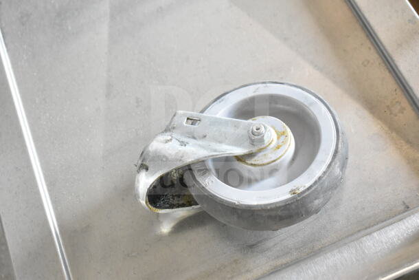 Commercial caster from a Blodgett Mark V-100 oven stand, showing signs of wear, metal frame and rubber wheel.